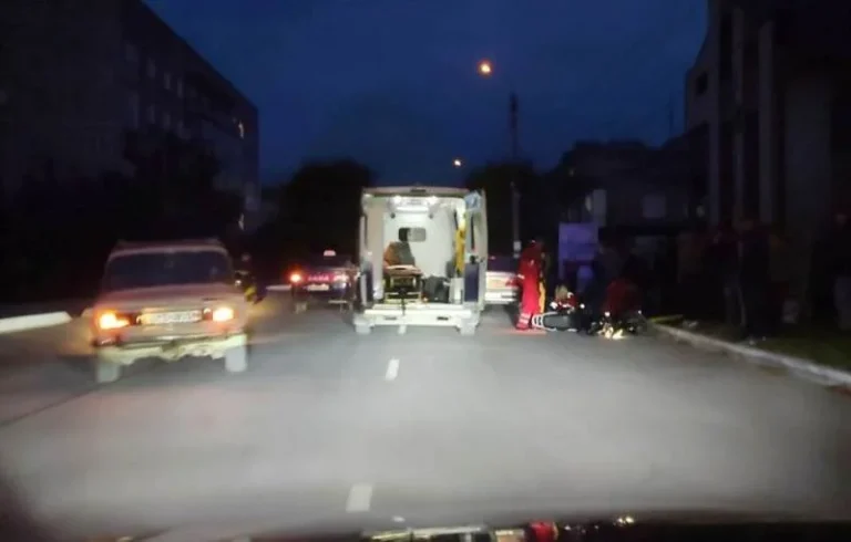Нічна вулиця з відкритою каретою швидкої, білим авто та людьми біля мотоцикла