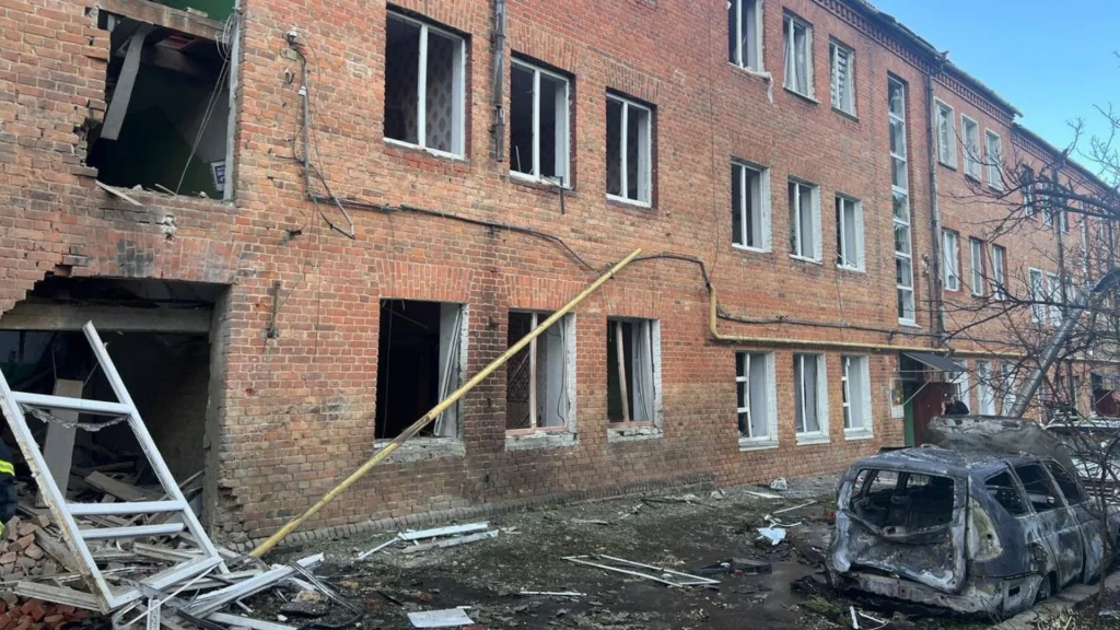 Пошкоджений цегляний будинок зі зруйнованими вікнами і згорілим автомобілем після вибуху